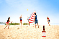 Wide advertising photograph of friends playing volleyball on the beach with a beverage bottle in the foreground.