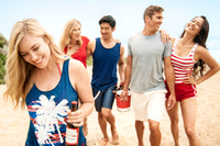 Lifestyle advertising photograph of four friends walking together on the beach while carrying bottled drinks.