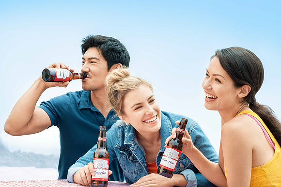 Lifestyle photograph of three friends laughing together with bottled drinks at the beach.