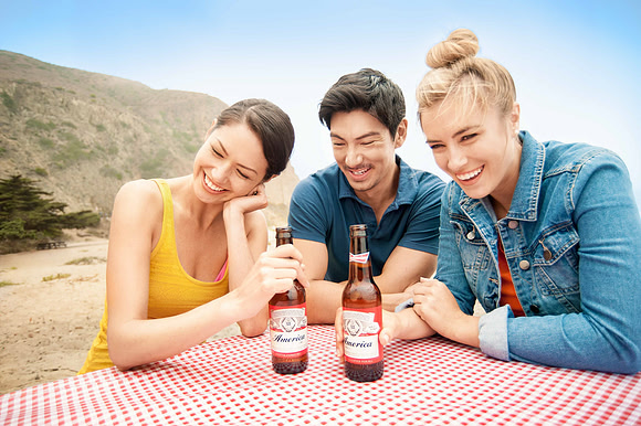 Beach advertising image of three friends seated at a picnic table with bottled beverages.