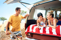 Lifestyle campaign photograph of friends gathered around the open rear of a vintage van at the beach.