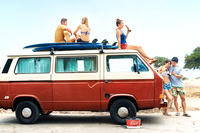Wide lifestyle photograph of friends sitting on and around a vintage van during a beach outing.