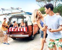 Lifestyle advertising photograph of a smiling couple holding a bottled drink beside a vintage beach van.