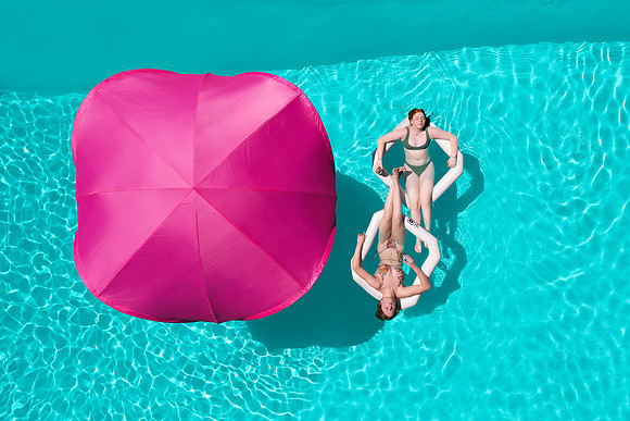 Overhead lifestyle photograph of a bright pink pool canopy and two people on a white float.