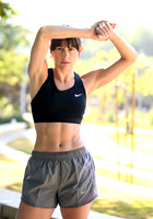 Outdoor fitness portrait of a woman in black athletic wear shielding her eyes from the sun.