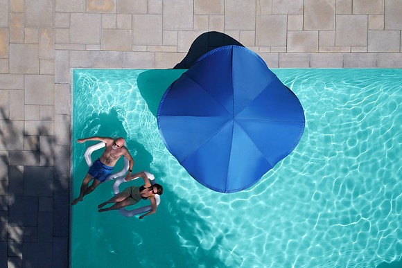 Overhead lifestyle photograph of a blue pool canopy beside swimmers in a clear backyard pool.