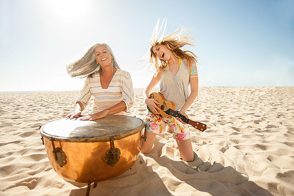 Lifestyle photograph of two women playing a large hand drum together on the beach.