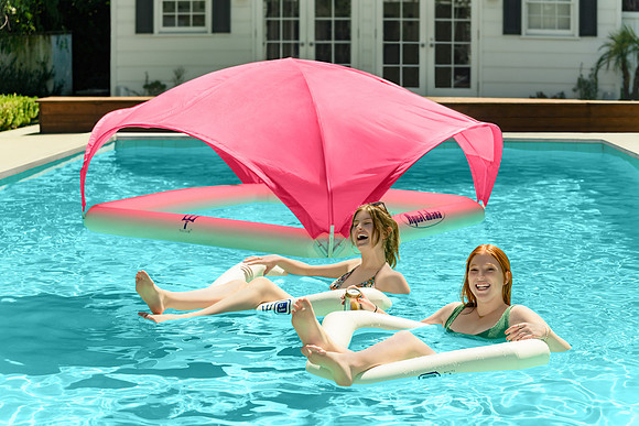 Pool advertising photograph of two women lounging on floats beneath a bright pink pool canopy.