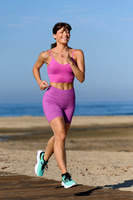 Active lifestyle photograph of a woman running along the beach in bright athletic wear.