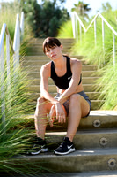 Fitness lifestyle portrait of a woman in black workout clothing seated on landscaped outdoor steps.