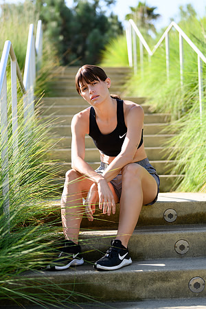 Fitness lifestyle portrait of a woman in black workout clothing seated on landscaped outdoor steps.