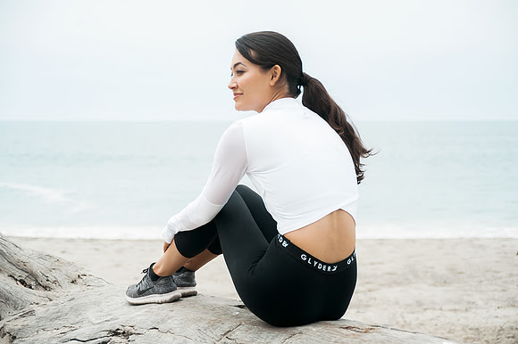 Lifestyle fitness photograph of a woman seated on a beach rock in black-and-white workout clothing.