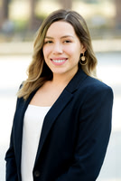 Professional outdoor headshot of a woman in a navy blazer over a white top.