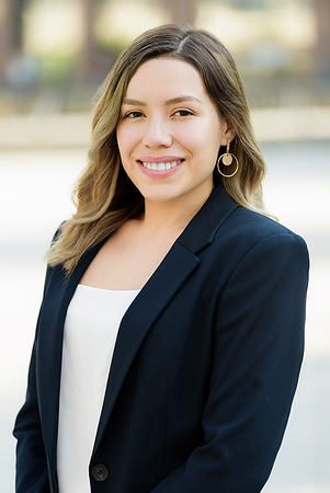 Professional outdoor headshot of a woman in a navy blazer over a white top.