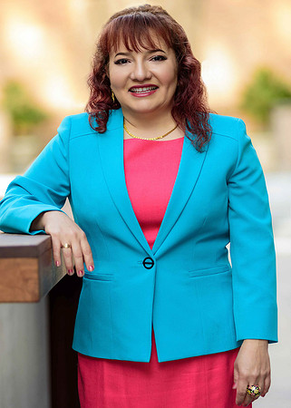 Professional outdoor portrait of a smiling woman in a turquoise blazer and bright pink top.