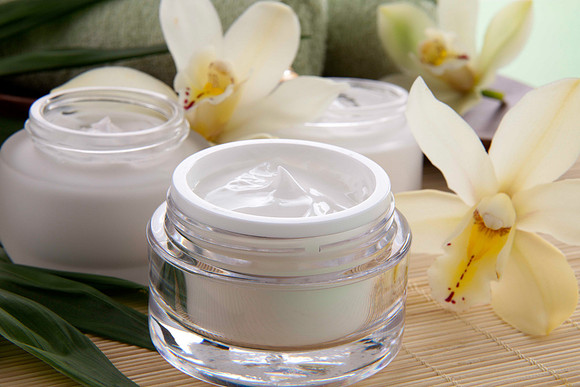 Beauty product still life of open cream jars arranged with white orchids and green leaves.