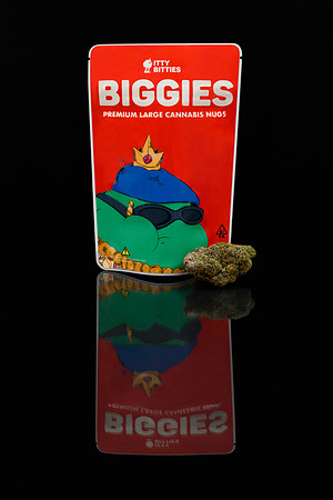 Dark studio product photograph of a Biggies cannabis package displayed with a flower bud on a reflective surface.
