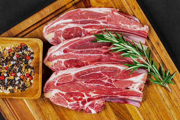Overhead commercial food photograph of raw lamb chops arranged with rosemary and mixed seasoning.