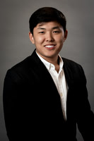 Studio headshot of a smiling man in a black suit against a neutral gray background.