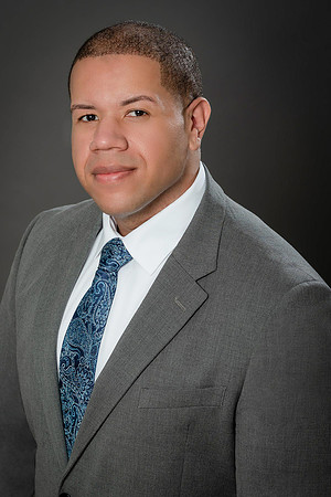Professional studio headshot of a man in a gray suit and patterned blue tie.