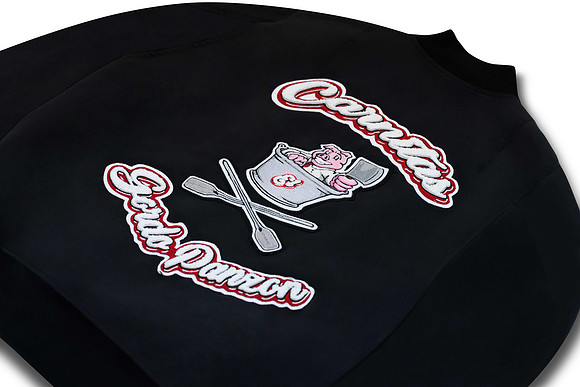Close product detail photograph of embroidered lettering and graphic artwork on a black bomber jacket.