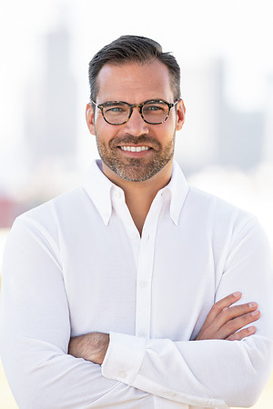 Business headshot of a man in a white shirt with arms crossed against a bright neutral background.
