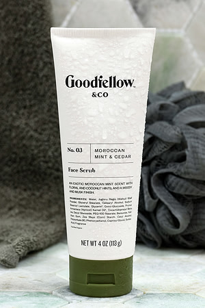Skincare product photograph of a Goodfellow & Co face scrub tube covered in water droplets beside a dark towel.