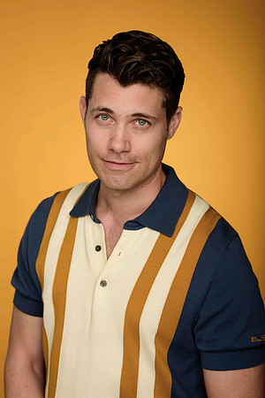 Editorial portrait of a man in a retro striped shirt against a warm golden background.