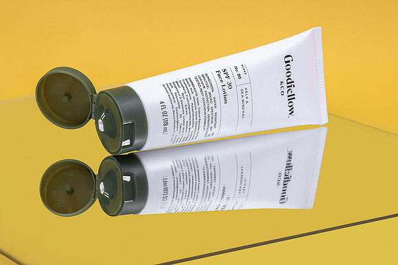 Creative product photograph of Goodfellow & Co face lotion lying open on a reflective yellow surface.