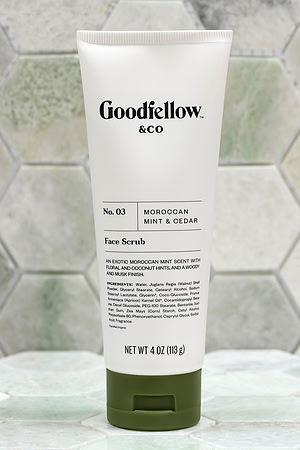 Product photograph of a Goodfellow & Co face scrub tube standing against pale geometric tile.