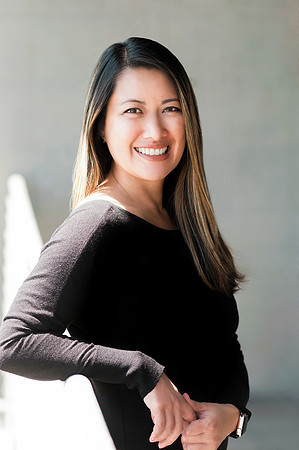 Professional portrait of a smiling woman in a black top posed near a modern interior wall.