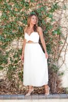Full-length editorial portrait of a woman in a white summer dress standing against ivy-covered brick.