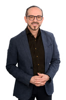 Studio business portrait of a man in glasses and a dark blazer standing against white.