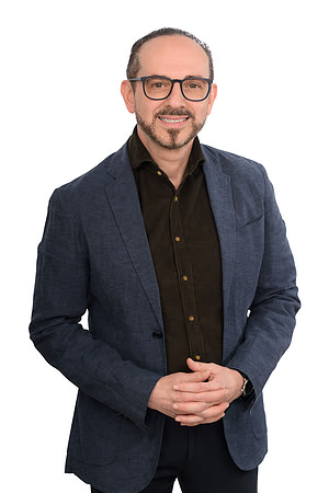 Studio business portrait of a man in glasses and a dark blazer standing against white.