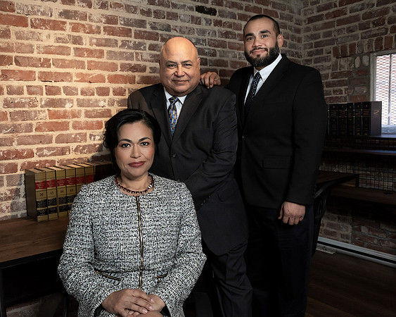 Professional group portrait of three businesspeople in an office with a brick wall backdrop.