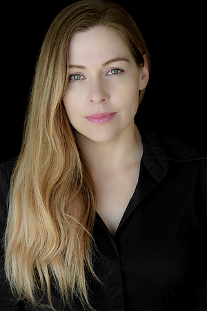 Low-key professional headshot of a woman in black against a dark background.
