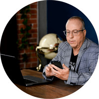 Professional branding image of the Technolene founder using a smartphone beside a laptop in an office setting.