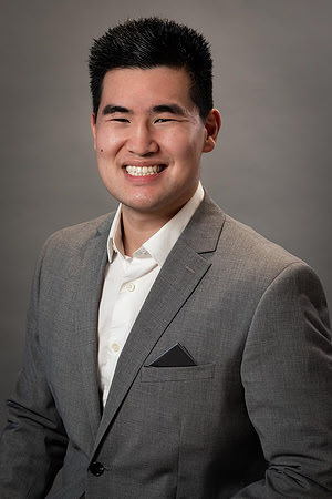 Studio business headshot of a smiling man in a gray suit against a neutral gray background.