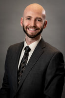 Studio business headshot of a smiling bald man in a dark suit and patterned tie.