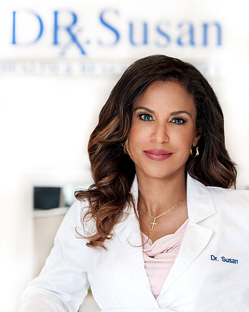 Professional headshot of a woman in a white medical coat with a blurred clinic sign behind her.