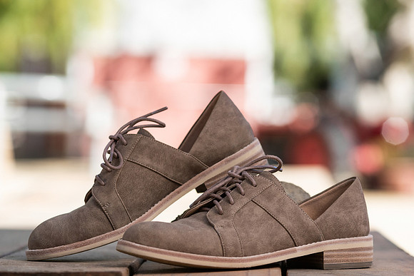 Commercial footwear photograph of taupe lace-up shoes styled outdoors with a softly blurred background.