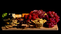 Commercial food photograph of a charcuterie board with cheeses, cured meats, fruit, crackers, and nuts.