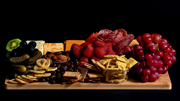 Commercial food photograph of a charcuterie board with cheeses, cured meats, fruit, crackers, and nuts.