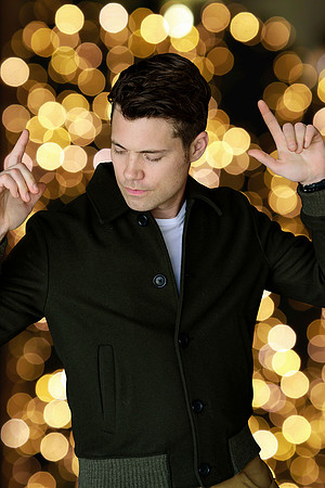 Editorial portrait of a man in sunglasses against a background of warm circular lights.