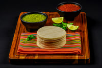 Commercial food photograph of stacked tortillas with bowls of green and red salsa, lime, and cilantro.