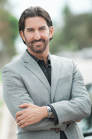 Professional outdoor portrait of a man in a light gray blazer with arms crossed.