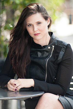 Professional portrait of a woman in a black jacket seated outdoors at a table.