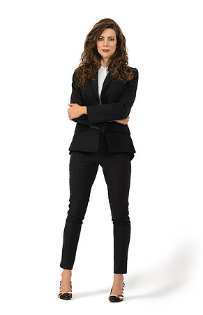 Full-length studio portrait of a brunette woman standing confidently in a black suit on white.