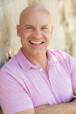 Professional lifestyle headshot of a smiling bald man wearing a pink polo shirt.