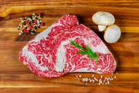 Overhead food photograph of heavily marbled raw beef cuts with mushrooms and coarse seasoning on wood.